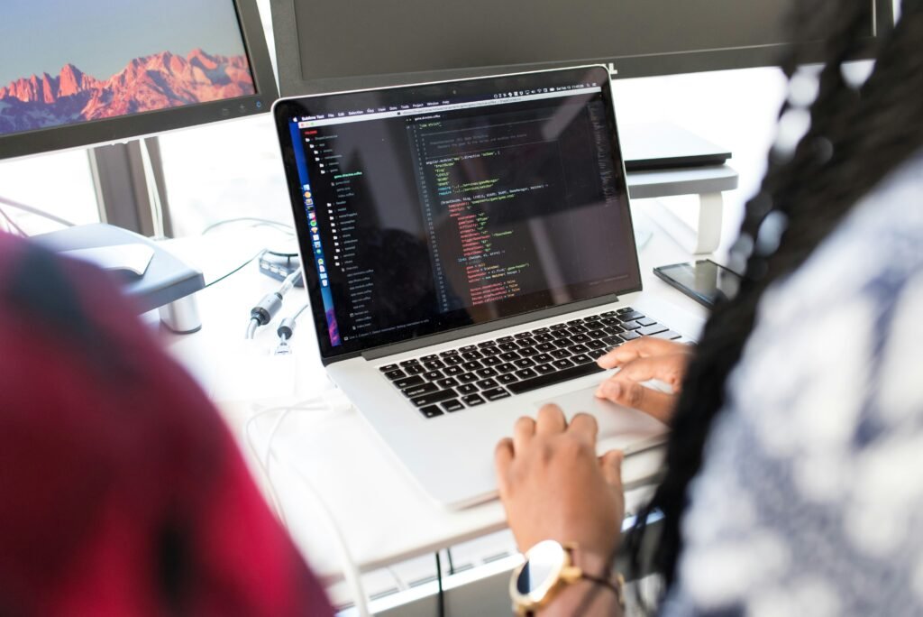 Close-up of a programmer coding on a laptop with multiple screens in a modern office setting. Caption: Software development in action – building and optimizing custom applications.